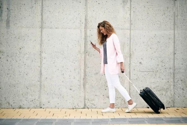 妇女携带行李和使用智能手机, 而步行到日 — 图库照片