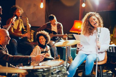 Caz Orkestrası Konser için hazırlanıyor. Ön plan kadının grubun geri kalanı şarkı bas gitar, clavier ve akustik gitar oynamak. Ev müzik stüdyosu iç.