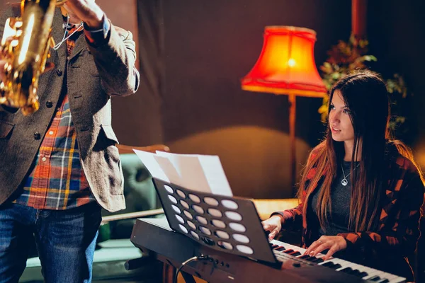 Calvo caucasico uomo suonare il sassofono in casa studio mentre la giovane donna di talento che gioca più clavier . — Foto Stock