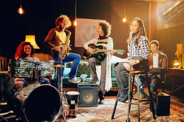 Prática de banda em estúdio em casa. Mulher cantando enquanto o resto da banda tocando instrumentos . — Fotografia de Stock