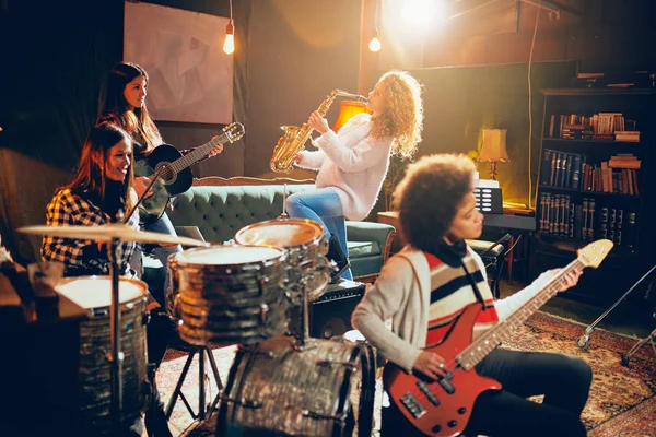 Des filles qui jouent du jazz. Au premier plan une femme joue de la guitare basse et en arrière-plan deux autres jouent du saxophone et de la batterie. Accueil studio intérieur . — Photo
