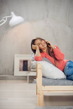 Rahat yatak odasında yatakta yalan ve Evet sevimli gülümseyen beyaz esmer giyinmiş.