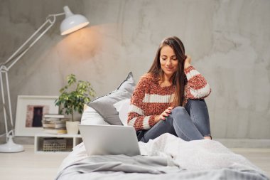 Muhteşem gülümseyen beyaz esmer uzun saçlı yatakta yatak odasında oturma ve tarassut video üstünde laptop.