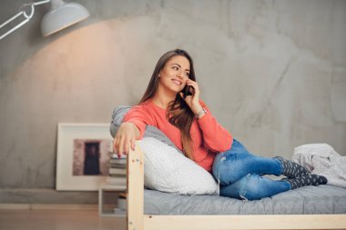 Rahat yatak odasında yatakta yalan ve Evet sevimli gülümseyen beyaz esmer giyinmiş.