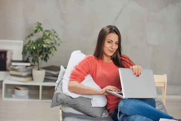 Schöne lächelnde kaukasische Brünette sitzt auf dem Bett im Schlafzimmer und mit Laptop. — Stockfoto