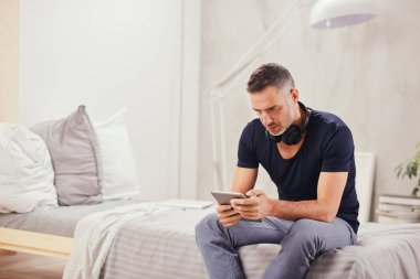 Beyaz adam yatakta yatak odasında oturma ve tablet kullanarak kırklı.