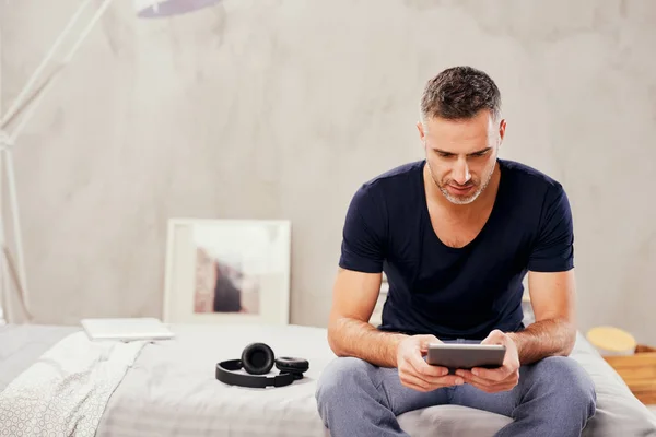 Caucásico hombre de cuarenta años sentado en la cama en el dormitorio y el uso de la tableta . —  Fotos de Stock
