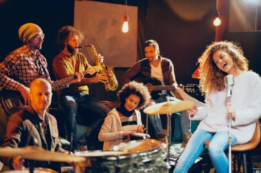 Caz Orkestrası Konser için hazırlanıyor. Ön plan kadının grubun geri kalanı şarkı bas gitar, clavier ve akustik gitar oynamak. Ev müzik stüdyosu iç.