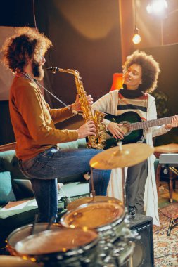 Karışık ırk kadın adam saksafon oynamaya akustik gitar çalmak. Ev stüdyosu iç.