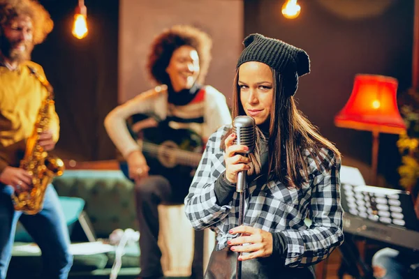 Band practice in home studio. Woman singing while rest of the band playing instruments.