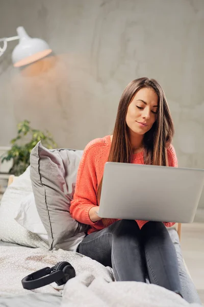 Vackra kaukasiska brunett sitter på sängen i sovrummet och använder bärbar dator. — Stockfoto