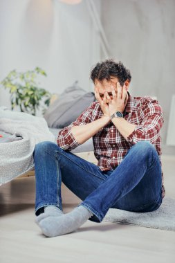 Ekose gömlek ve yatak odasında katta oturan ve yüzünde elele kot şirin Arap adam. Erkekler sorunları kavramı.