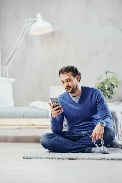 매력적인 아랍 남자 옷 캐주얼 침실에서 바닥에 앉아 읽기 또는 메시지를 보내는 스마트 휴대 전화를 사용 하 여. — 스톡 사진