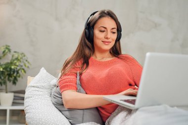 Müzik dinleme ve yatak odasında yatağın üstünde otururken dizüstü kullanarak muhteşem beyaz esmer.