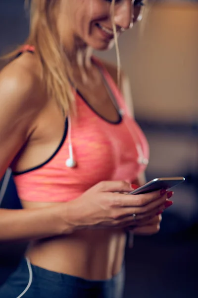 Primer plano de la mujer que usa el teléfono inteligente para enviar mensajes de texto / lectura mientras está de pie en el gimnasio. concepto de estilo de vida saludable . — Foto de Stock