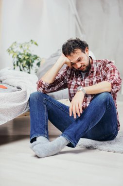 Kot pantolon ve yatak odasında katta oturan ve kafa tutan ekose gömlek çekici Arap adam. Erkekler sorunları kavramı.