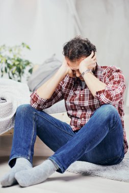 Kot pantolon ve yatak odasında katta oturan ve kafa tutan ekose gömlek çekici Arap adam. Erkekler sorunları kavramı.