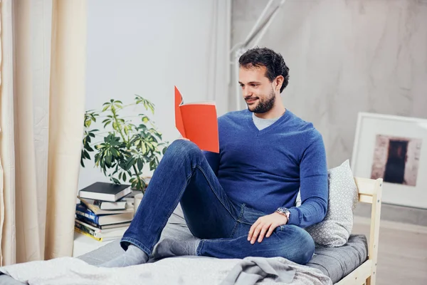 Vrolijke schattig Arabische man gekleed casual boek lezen en ontspannen zittend op het bed in de slaapkamer. — Stockfoto