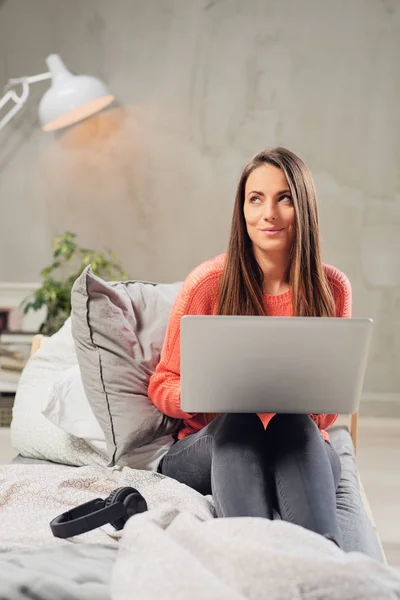 Vackra kaukasiska brunett sitter på sängen i sovrummet och använder bärbar dator. — Stockfoto