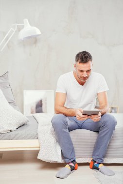 Beyaz adam yatakta yatak odasında oturma ve tablet kullanarak kırklı.