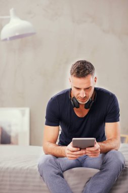 Beyaz adam yatakta yatak odasında oturma ve tablet kullanarak kırklı.