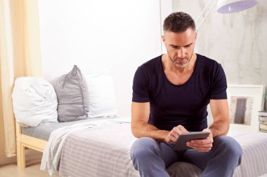 Beyaz adam yatakta yatak odasında oturma ve tablet kullanarak kırklı.