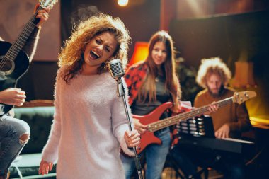 Grup çalışması göstermek için. Mikrofon tutan ve adam akustik gitar çalmak arka planda şarkı kıvırcık saçlı kadın. Ev stüdyosu iç.