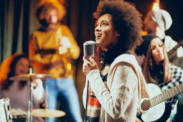 Gemengd ras vrouw zingen. In achtergrond band spelen van instrumenten. Home studio interieur. — Stockfoto