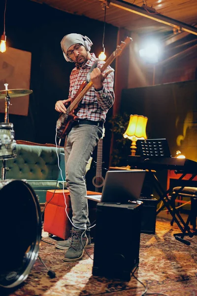Musicista caucasico concentrato che suona il basso con le cuffie sulle orecchie. Lunghezza totale . — Foto Stock