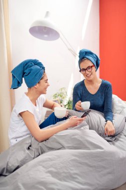 Teo güzel Kafkas kız yatak odasında yatakta oturan kafaları havlu ile, kahve içme ve dedikodu.