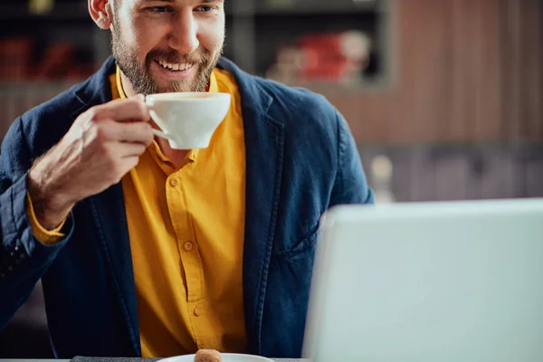 Närbild av skäggiga leende kaukasiska frilansare sitter i Café, dricka färskt kaffe och använda lapotp. — Stockfoto