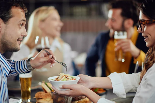 Amigos multiétnicos sentados no restaurante, bebendo álcool, conversando e comendo hambúrgueres para o jantar . — Fotografia de Stock