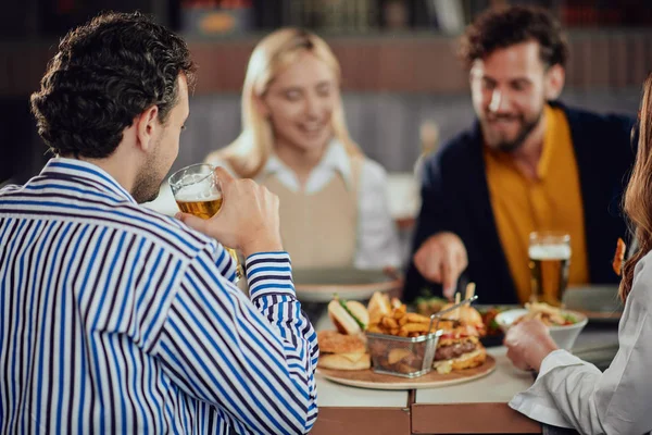 Amis multiethniques assis au restaurant, buvant de l'alcool, bavardant et ayant des hamburgers pour le dîner . — Photo