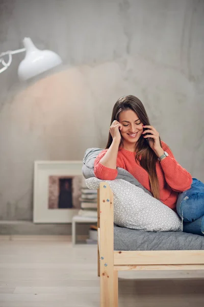 Encantadora morena caucásica sonriente vestida casual acostada en la cama en el dormitorio y hablando por teléfono . — Foto de Stock