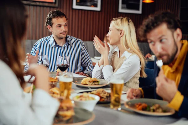 Amis multiethniques assis au restaurant, buvant de l'alcool, bavardant et ayant des hamburgers pour le dîner . — Photo
