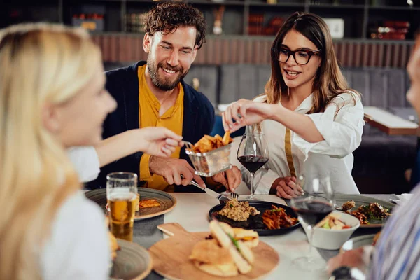 Multietnické přátele, kteří sedí v restauraci, konzumují alkohol, chatují a mají hamburgery na večeři. — Stock fotografie