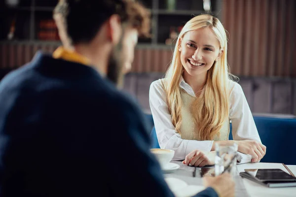Smiling Caucasian blonde businesswoman dressed smart casual discussing with her male colleague about project while sitting in coffe shop. — Stock Photo, Image