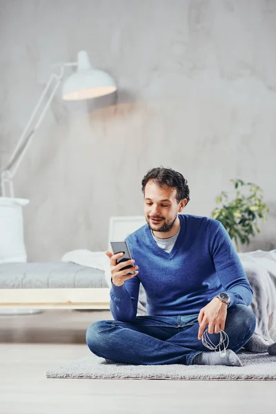 Attractive arab man dressed casual sitting on the floor in bedroom and using smart phone for reading or sending message. — Stock Photo, Image