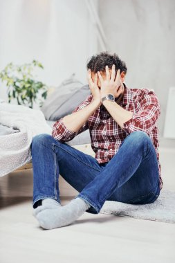 Kot pantolon ve yatak odasında katta oturan ve kafa tutan ekose gömlek çekici Arap adam. Erkekler sorunları kavramı.