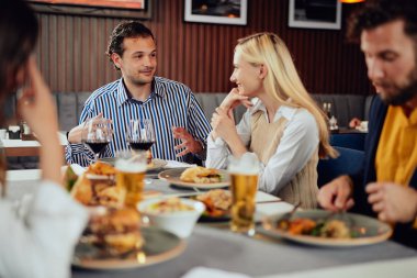 Çok ırklı arkadaşlar restoranda oturan, alkol içme, sohbet ve akşam yemeği için hamburger yeme.