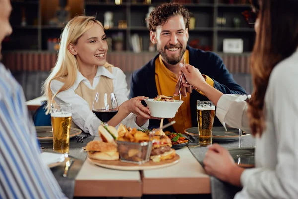 Multietniska vänner sitter på restaurang, dricka alkohol, chatta och ha hamburgare till middag. — Stockfoto