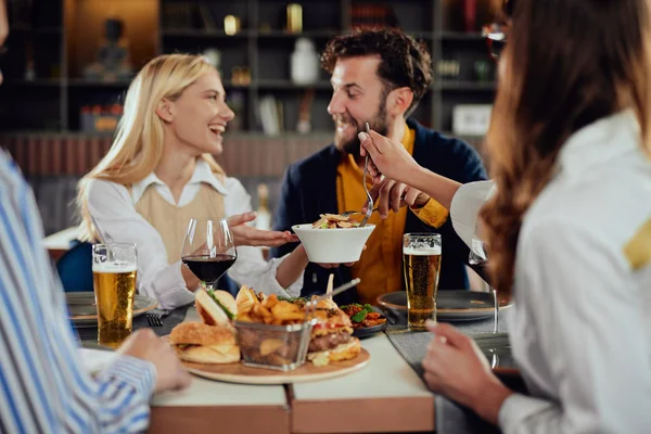 Multietniska vänner sitter på restaurang, dricka alkohol, chatta och ha hamburgare till middag. — Stockfoto