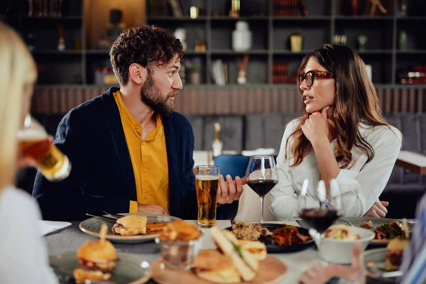 Amigos multiétnicos sentados en el restaurante, bebiendo alcohol, charlando y comiendo hamburguesas para cenar . — Foto de Stock