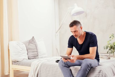 Beyaz adam yatakta yatak odasında oturma ve tablet kullanarak kırklı.