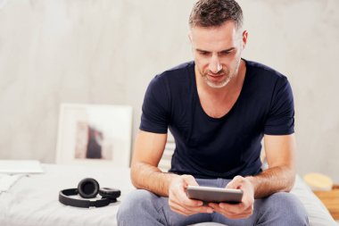 Beyaz adam yatakta yatak odasında oturma ve tablet kullanarak kırklı.