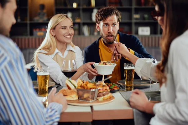 Amis multiethniques assis au restaurant, buvant de l'alcool, bavardant et ayant des hamburgers pour le dîner . — Photo