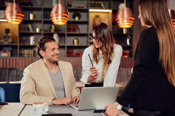 Arrtactive businessman dressed smart casual sitting in cafe. Around him his colleagues standing and  discussing about important project. — Stock Photo, Image