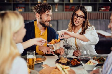 Çok ırklı arkadaşlar restoranda oturan, alkol içme, sohbet ve akşam yemeği için hamburger yeme.