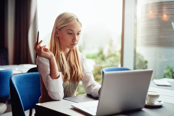Νέος Καυκάσιος ξανθιά επιχειρηματίας ντυμένος έξυπνη περιστασιακή χρησιμοποιώντας φορητό υπολογιστή και κρατώντας στυλό ενώ κάθονται σε καφετέρια. — Φωτογραφία Αρχείου