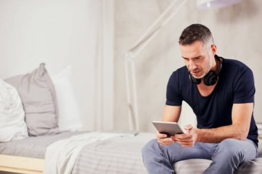 Beyaz adam yatakta yatak odasında oturma ve tablet kullanarak kırklı.